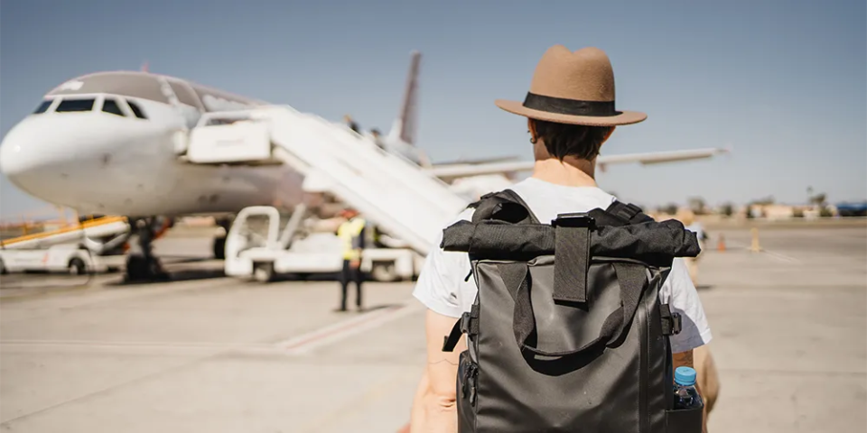 Alleine reisen / MLP Financify / Mann mit Rucksack vor einem Flugzeug