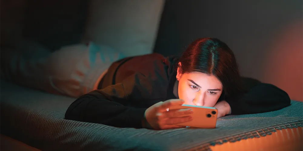 Junge Frau schaut auf Bett liegend auf Smartphone / MLP Financify