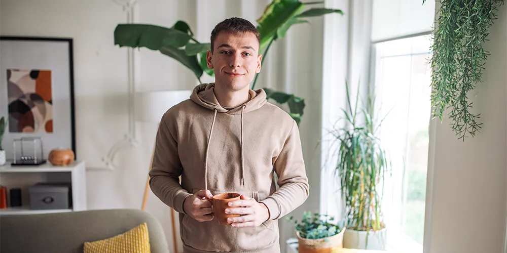 Energie sparen im Winter / MLP Finacify / Student mit Hoodie und warmer Tasse Tee in heller Wohnung