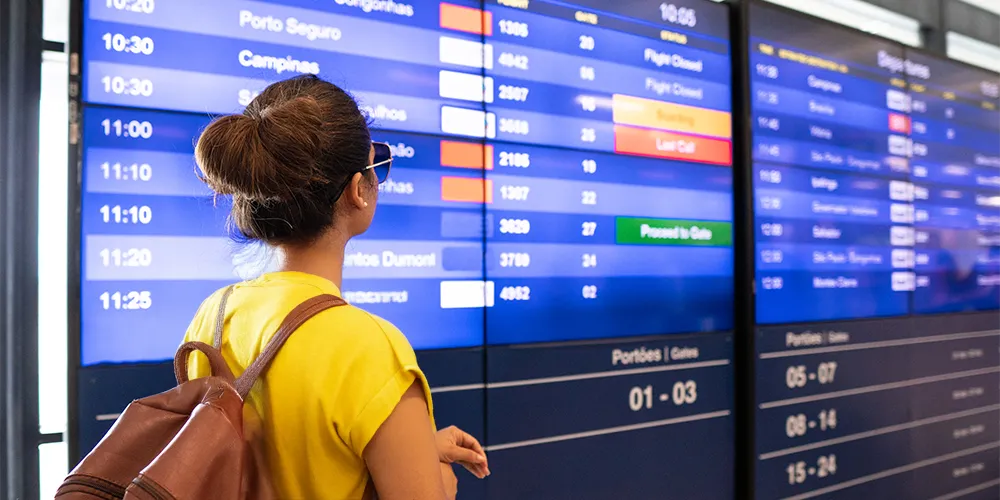 Was tun bei Flugausfall? / MLP Financify / Studentin steht vor Anzeigetafel am Flughafen und sieht ihren stornierten Flug