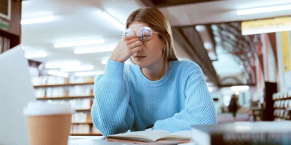 Mental Load: Was steckt hinter der unsichtbaren Mehrarbeit? / MLP Financify / Studentin beim Lernen in der Bib wirkt überfordert und gestresst