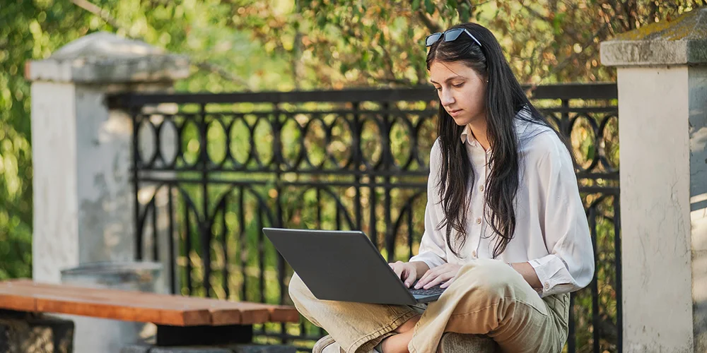Was im Internet geht und was nicht: So kannst du dich als Betroffener wehren / MLP Financify / Studentin sitzt auf einer Parkbank mit ihrem Laptop auf dem Schoß