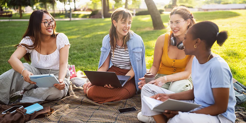 Netzwerke: Kontakte richtig knüpfen / MLP Financify / Gruppe Studierende sitzen zusammen auf Picknickdeck im Park und reden lachend miteinander
