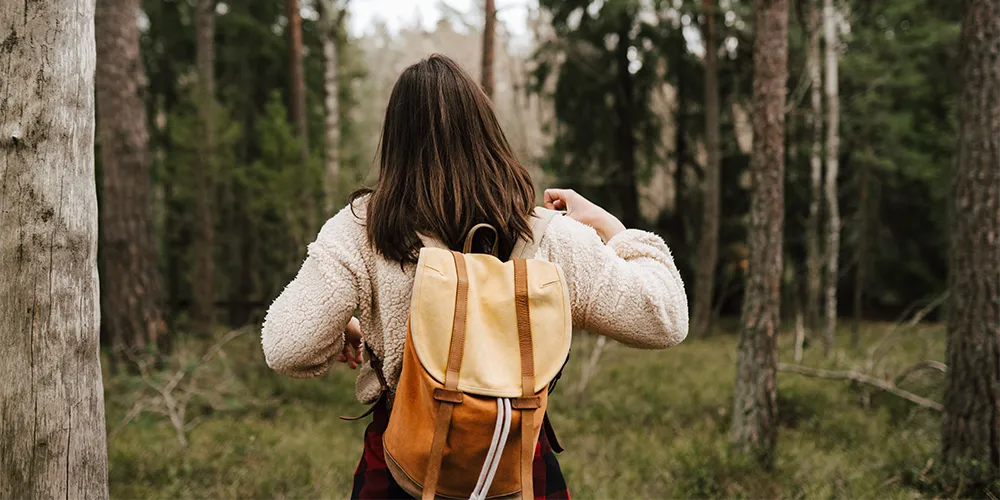 Eine junge Frau mit Rücksack auf dem Rücken läuft durch den Wald.