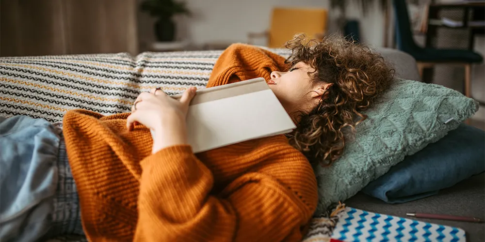 MLP Financify / Richtig Pause einlegen: Welcher Erholungstyp bist du? / Frau ist auf dem Sofa mit ihrem Buch eingeschlafen