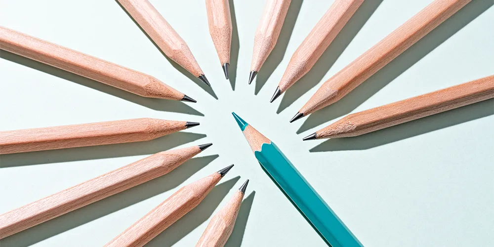 Perfektionismus überwinden: So wirst du gelassener / MLP Financify / Blauer Stift sticht in einen fast perfekten Kreis aus holzfarbenen Stiften
