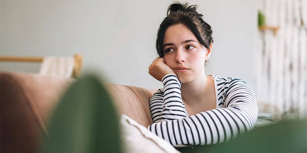 Stress und psychische Gesundheit im Studium / MLP Financify / Nachdenkliche Studentin auf Sofa