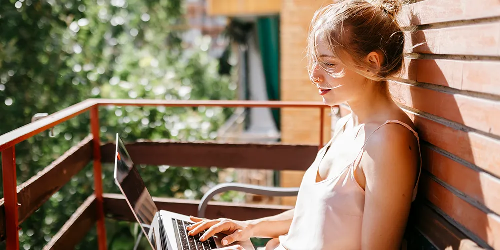Remote Jobs für Absolventen: Dein flexibler Karriereeinstieg / MLP Financify / Berufseinsteigerin sitzt mit Laptop auf dem Balkon und arbeitet.