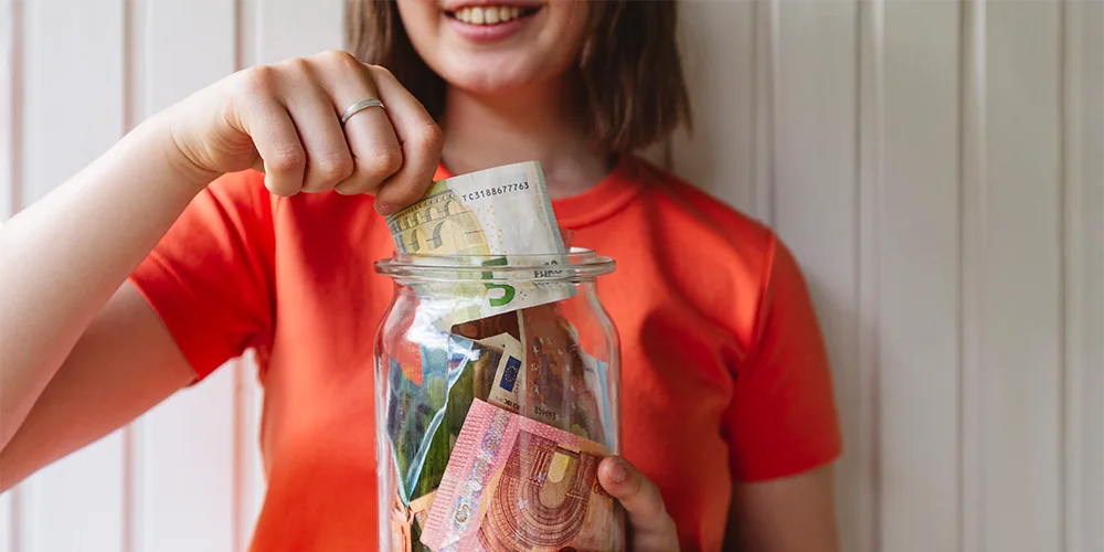 9 Spartipps für Studenten - wie Du als Student richtig Geld sparen kannst / MLP financify / Studentin legt Geld in eine Spardose