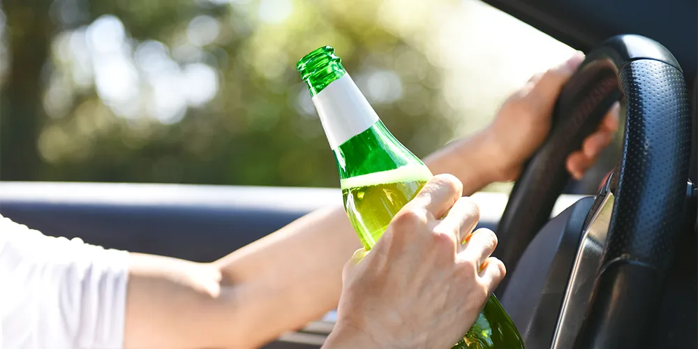 Führerschein weg? So bekommst du ihn wieder / MLP Financify / Student sitzt mit Bierflasche am Steuer seines Autos