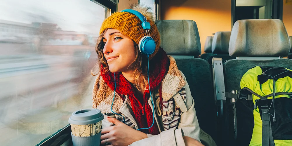 Günstig und nachhaltig reisen als Studierende / MLP Financify / Studierende sitzt in Herbstklamotten in der Bahn und schaut fröhlich aus dem Fenster