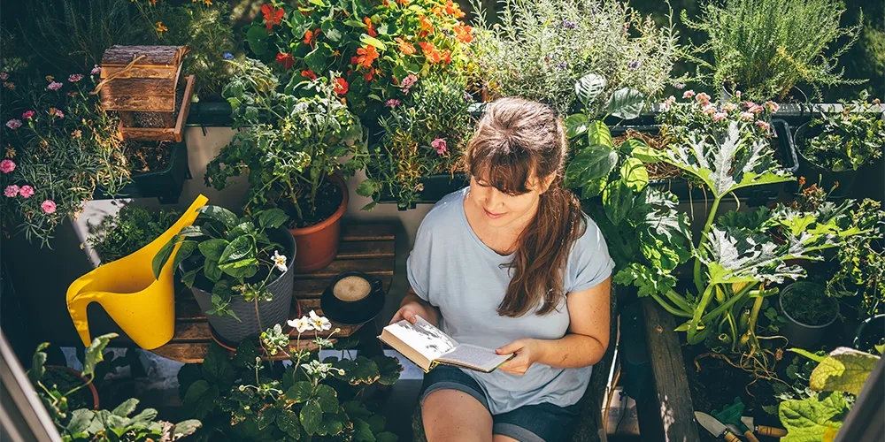 MLP Financify / Urban Gardening auf dem Balkon: günstig gärtnern im Studium / Studentin liest ei Buch auf ihrem Balkon-Garten
