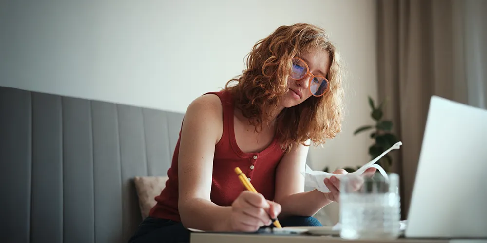 Vermögensaufbau im Studium / MLP Financify / Studentin plant ihren Vermögensaufbau am Schreibtisch.