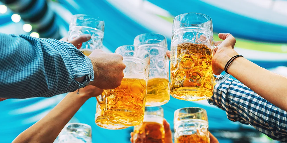 Im Bierzelt: Welche Versicherungen dich beim Feiern absichern / MLP Financify / Studierende stoßen mit Maßkrügen voll Bier an