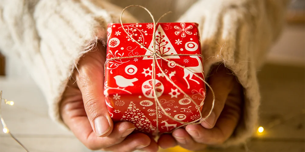 Weihnachten mit kleinem Budget: Spartipps für Studierende / MLP Financify / Frau hält rotes Geschenk in den Händen