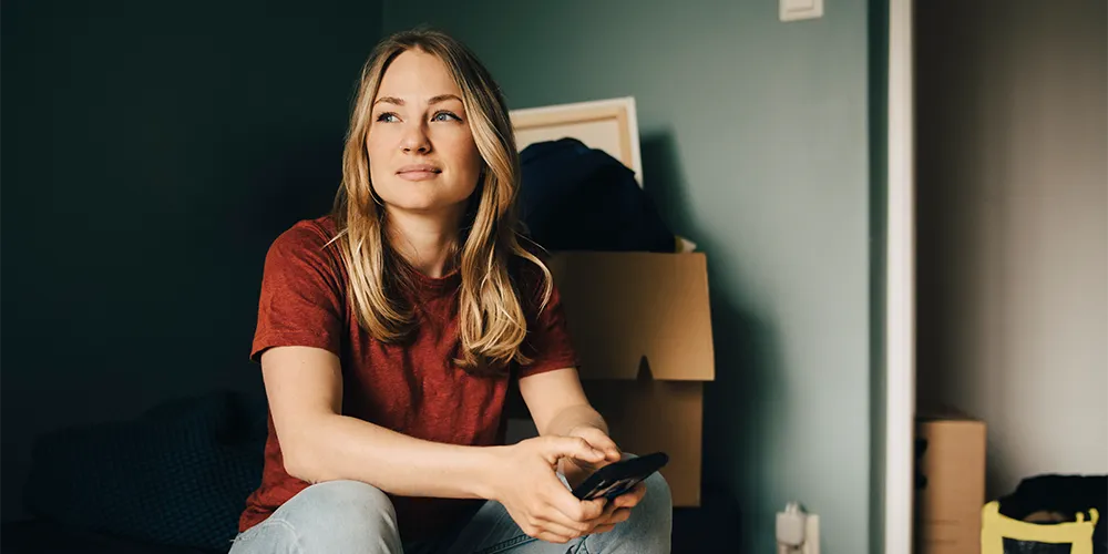 WG, eigene Wohnung oder Pendeln? – Wohnmodelle im Finanzcheck für Studierende und Berufseinsteiger / MLP Financify / Studentin in Wohnung mit Umzugskartons